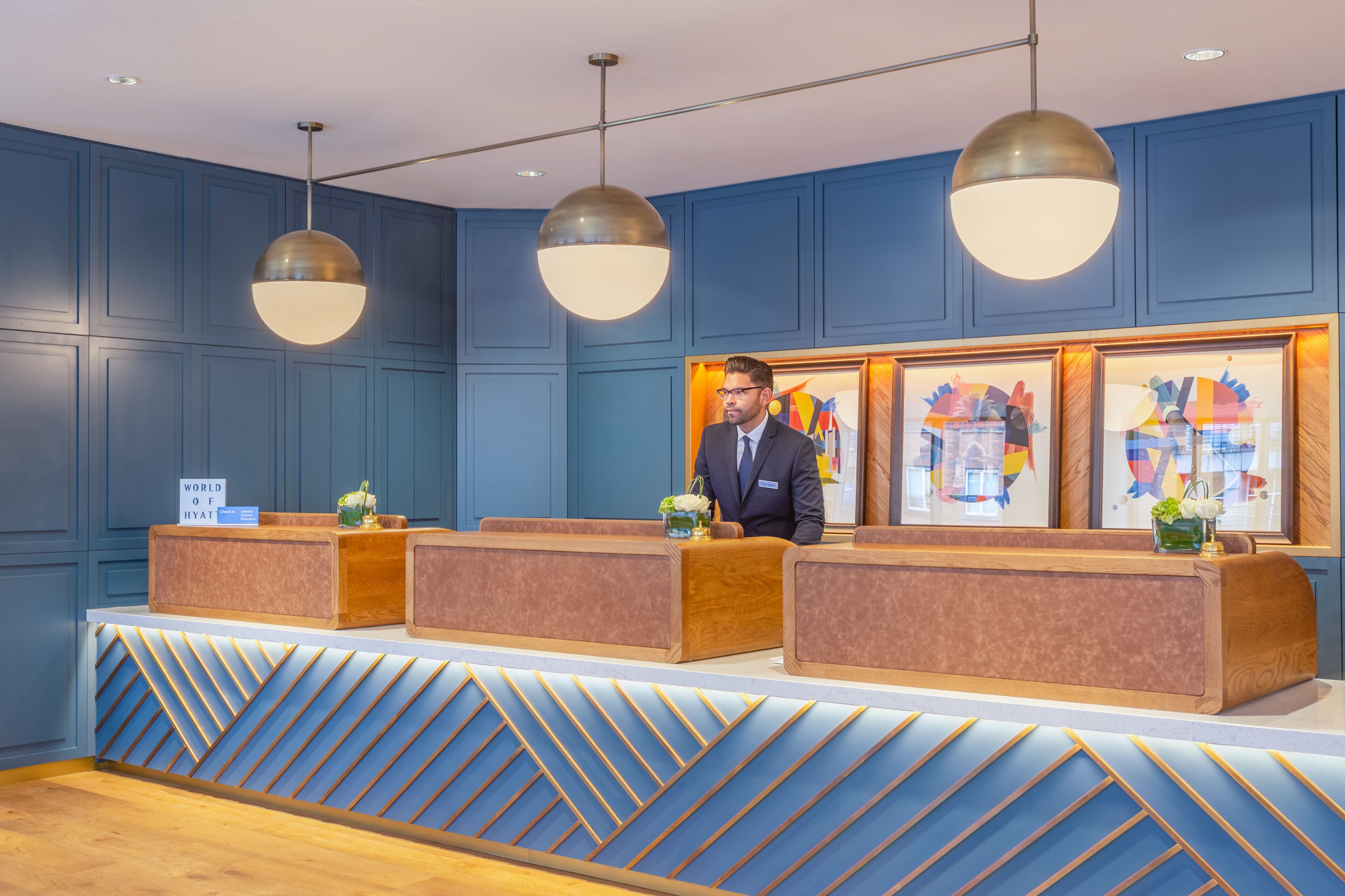 Zona de recepción de hotel con pared azul, tres mostradores y una recepcionista.