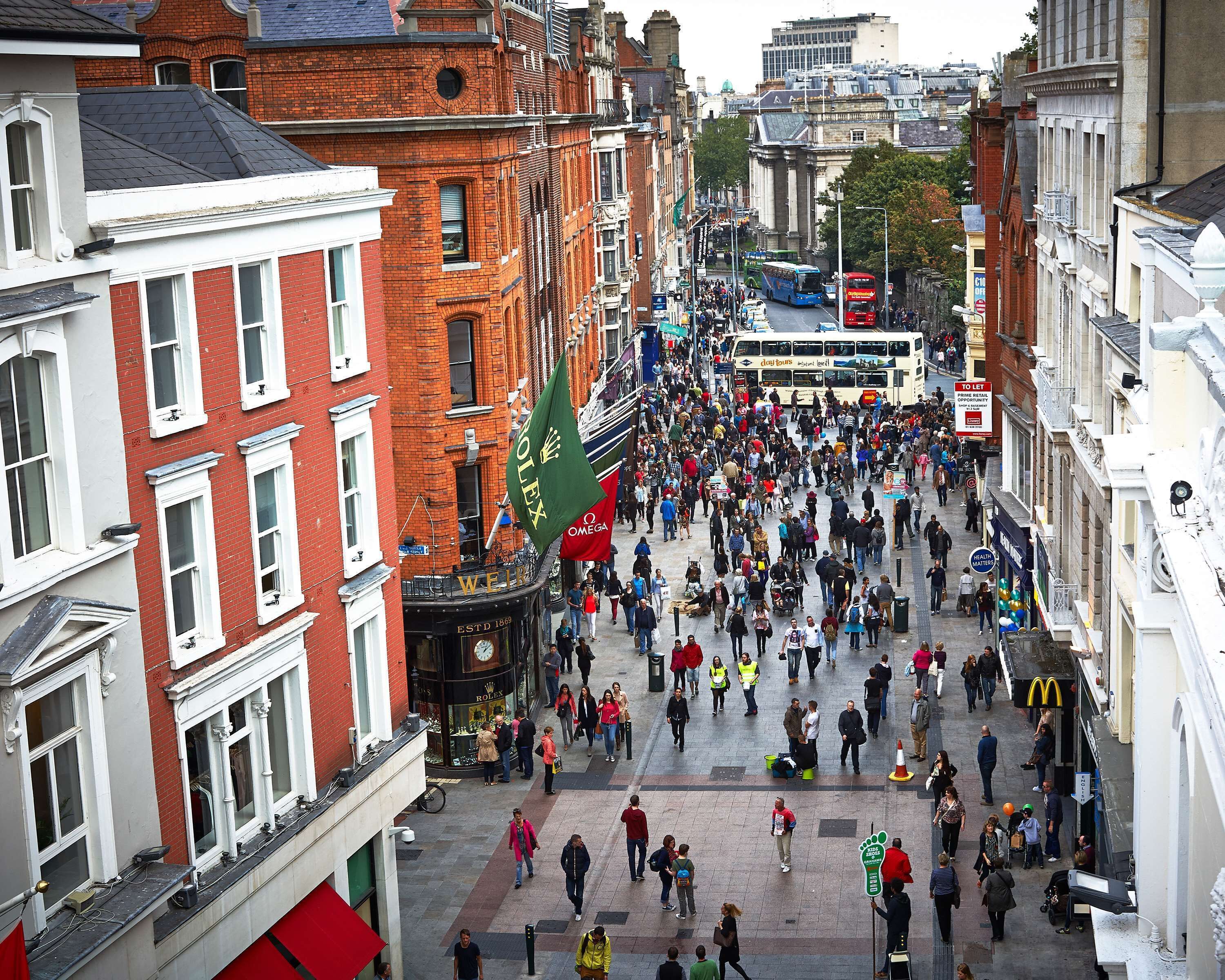 A busy urban street with pedestrians, historic buildings, and a double-decker bus.