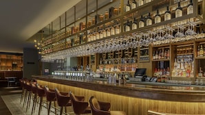 Een bar met een houten toonbank, diverse drankflessen en hangende wijnglazen.