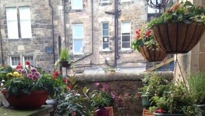 A small outdoor patio area with a wooden table and chairs, surrounded by potted plants and hanging planters. - Doune Guest House (St. Andrews)