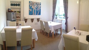 A dining area with white tables and chairs, a blue wall art piece, and a window with curtains. - Doune Guest House (St. Andrews)