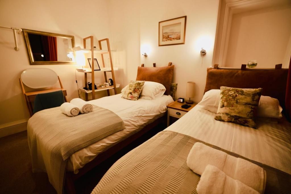 A hotel room with two beds, a desk, a chair, and a bedside table with a lamp.