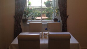 A dining area with a table and chairs, a window with curtains, and potted plants on the windowsill. - Doune Guest House (St. Andrews)