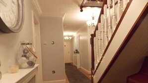 Un pasillo con una escalera de madera, un reloj y un jarrón decorativo.