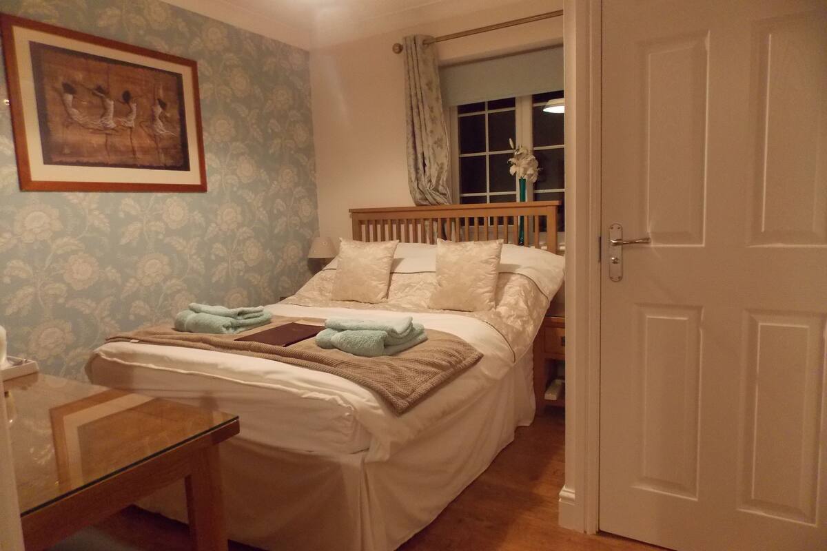 Una cama bien hecha con almohadas y una manta, una mesita de noche con una lámpara y un cuadro en la pared.