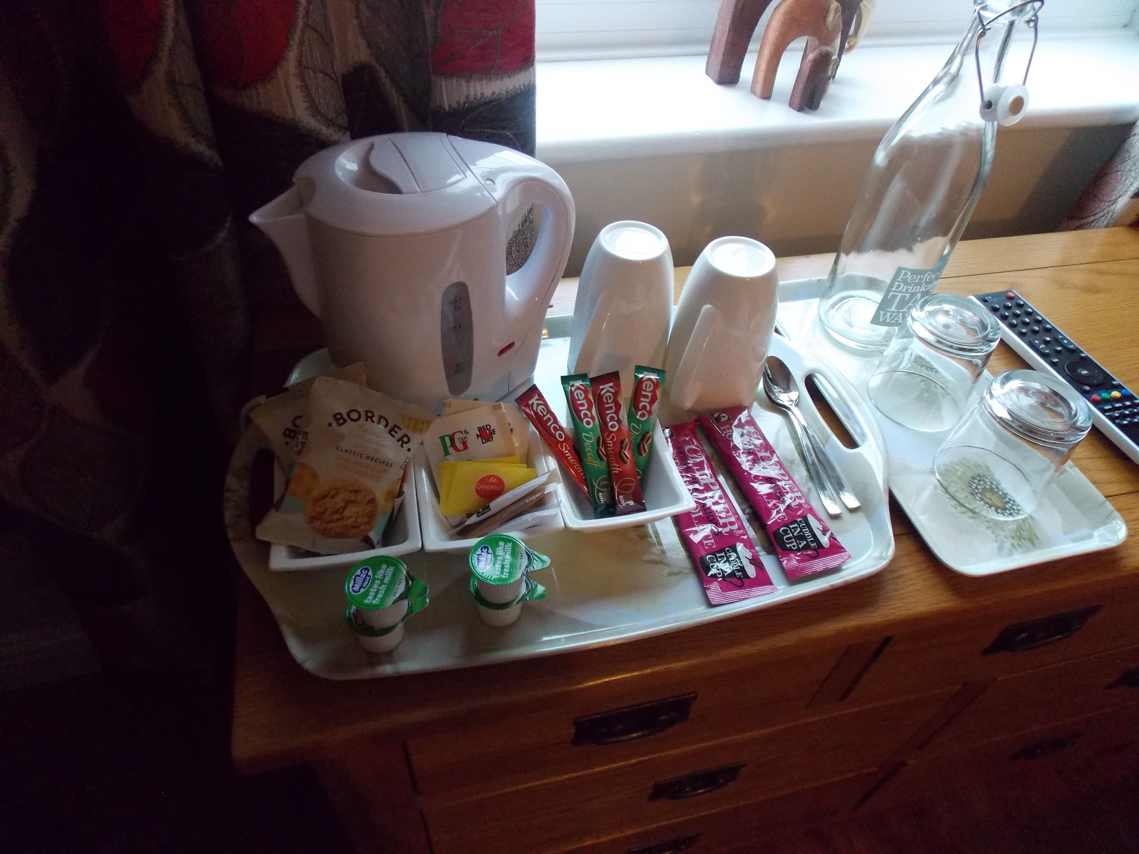 A tray with a coffee maker, tea cups, and various food items on a wooden table.