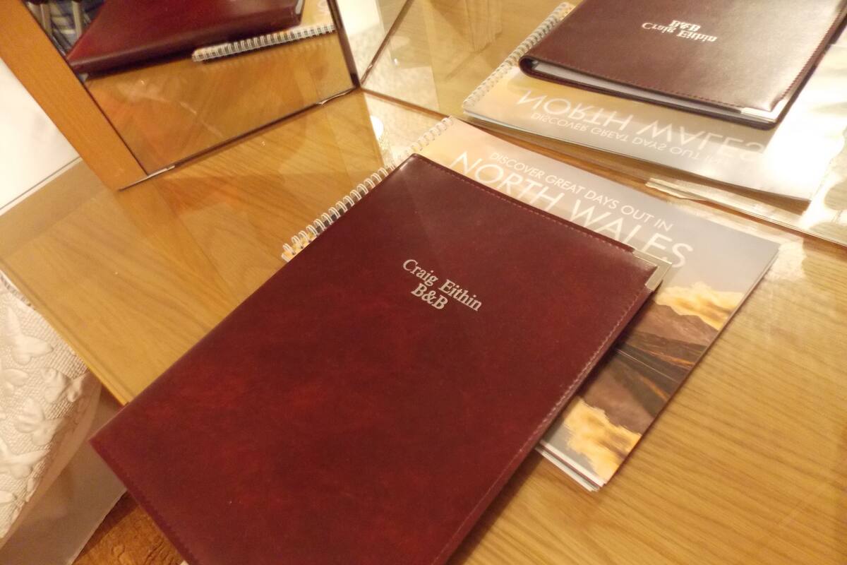 Un libro de tapa de cuero marrón con el título 'Craig Eithin B&B' sobre una mesa de madera.