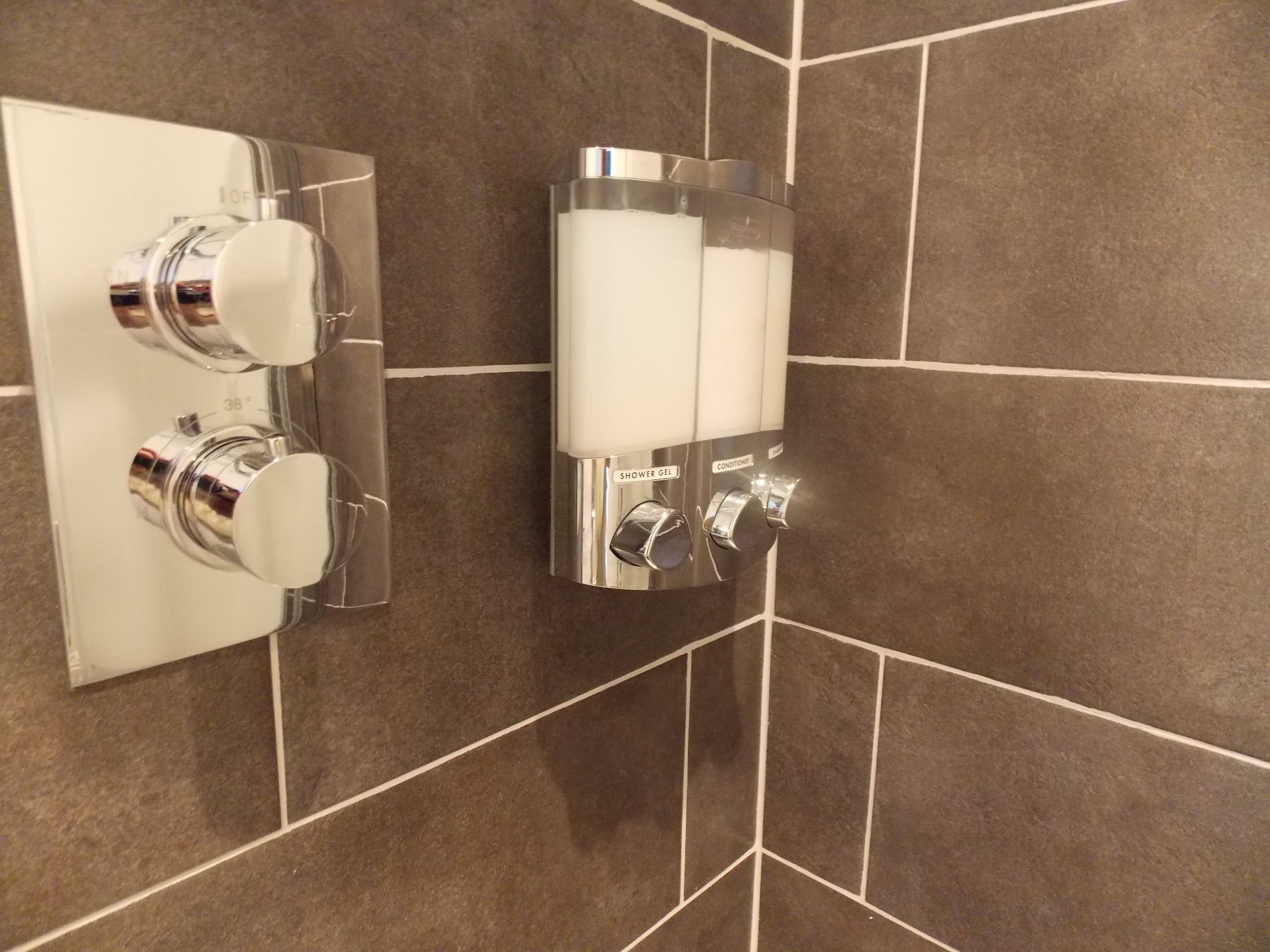 A bathroom with a shower control panel and a hand dryer.