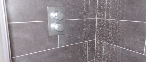 Una ducha con panel de control y pared de azulejos.