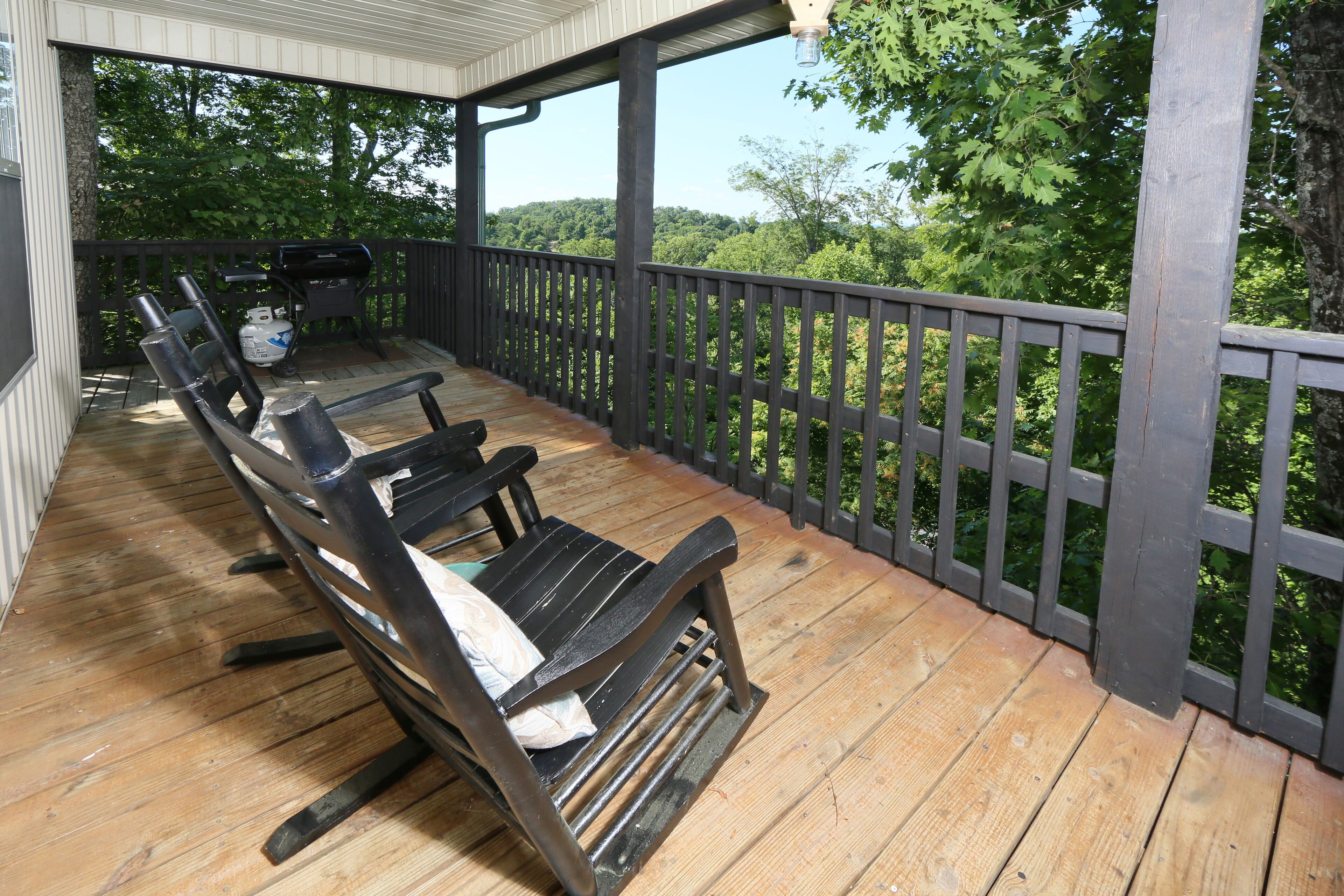 A wooden deck with a railing, outdoor seating, and a grill.