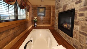 A bathroom with a bathtub, a stone wall, a fireplace, and a window with blinds. - Above It All - Four Bedroom Cabin (Gatlinburg)