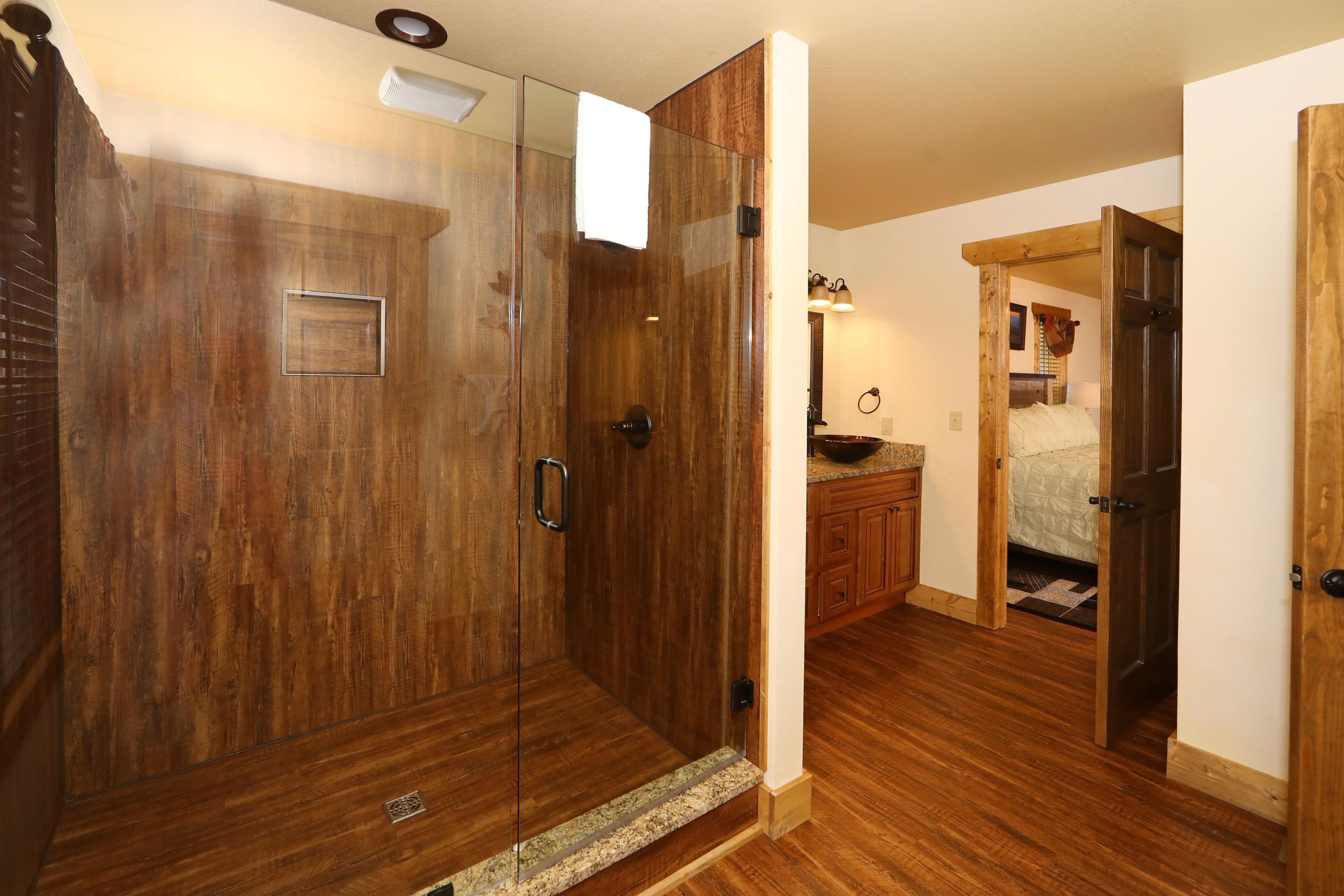 Une douche à l’italienne avec une porte en verre, un revêtement mural en bois et une petite grille de ventilation.