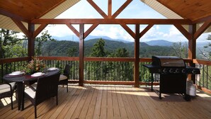 A covered outdoor deck with a wooden table and chairs, a grill, and a scenic mountain view. - Above It All - Four Bedroom Cabin (Gatlinburg)