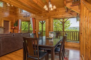 Relax in a cozy cabin-style interior with a dining area, comfortable sofa, and large windows offering a view of the surrounding landscape.