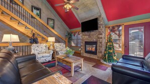 A cozy living room with a fireplace, leather sofas, a wooden coffee table, and a staircase with a red ceiling. - Aqua Paradise - Six Bedroom Chalet (Gatlinburg)