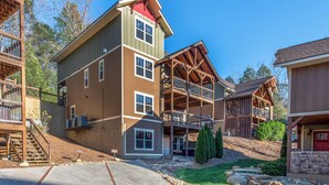 A multi-story building with a wooden exterior, a covered porch, and a staircase leading to the entrance. - Aqua Paradise - Six Bedroom Chalet (Gatlinburg)