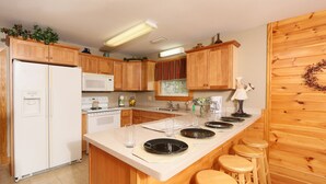 A kitchen with wooden cabinets, a refrigerator, a microwave, a sink, and a bar area with stools. - Pinnacle View 7A - Three Bedroom Chalet (Pigeon Forge)