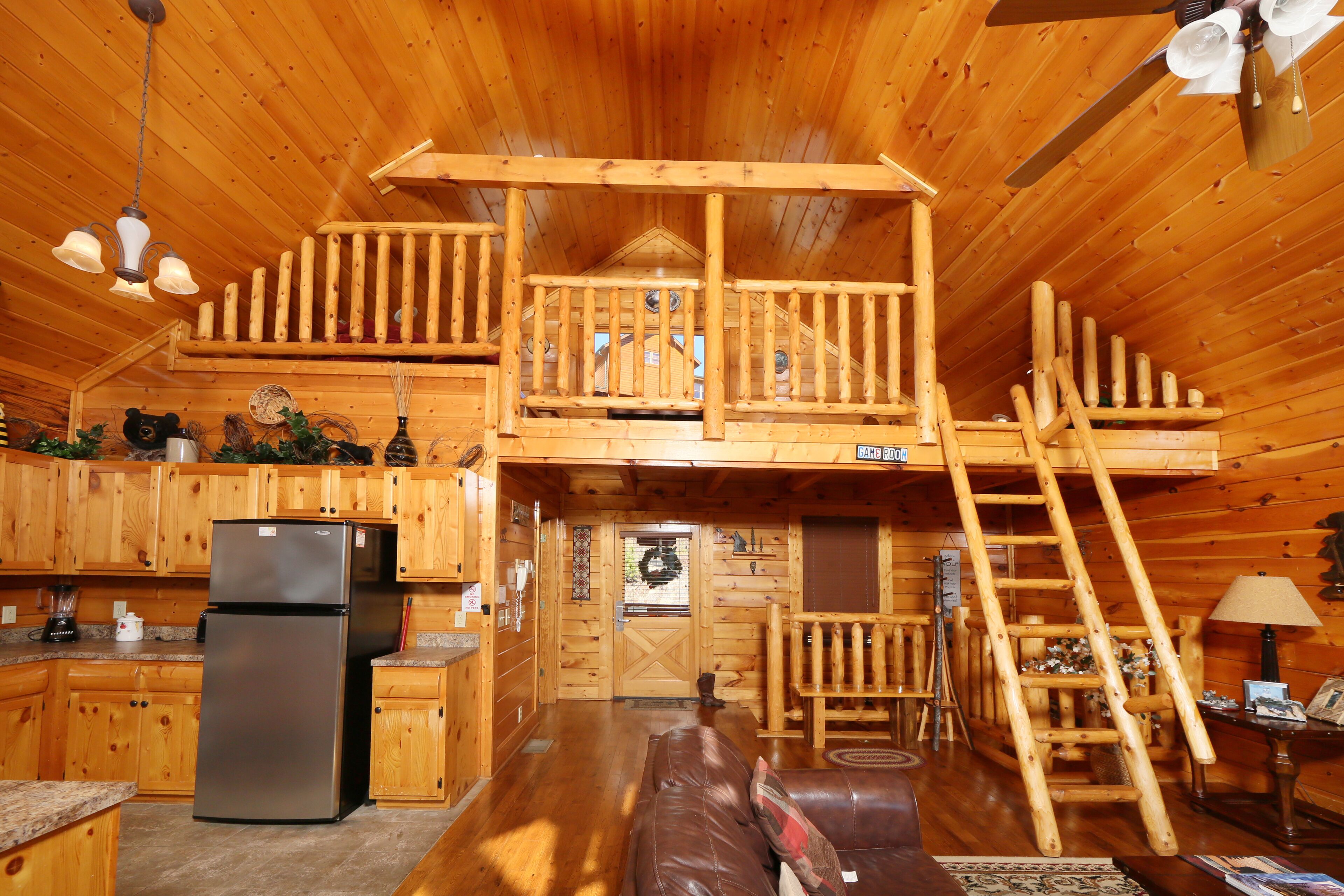 A cabin with a wooden interior, a kitchen with a refrigerator, a wooden staircase, and a balcony.