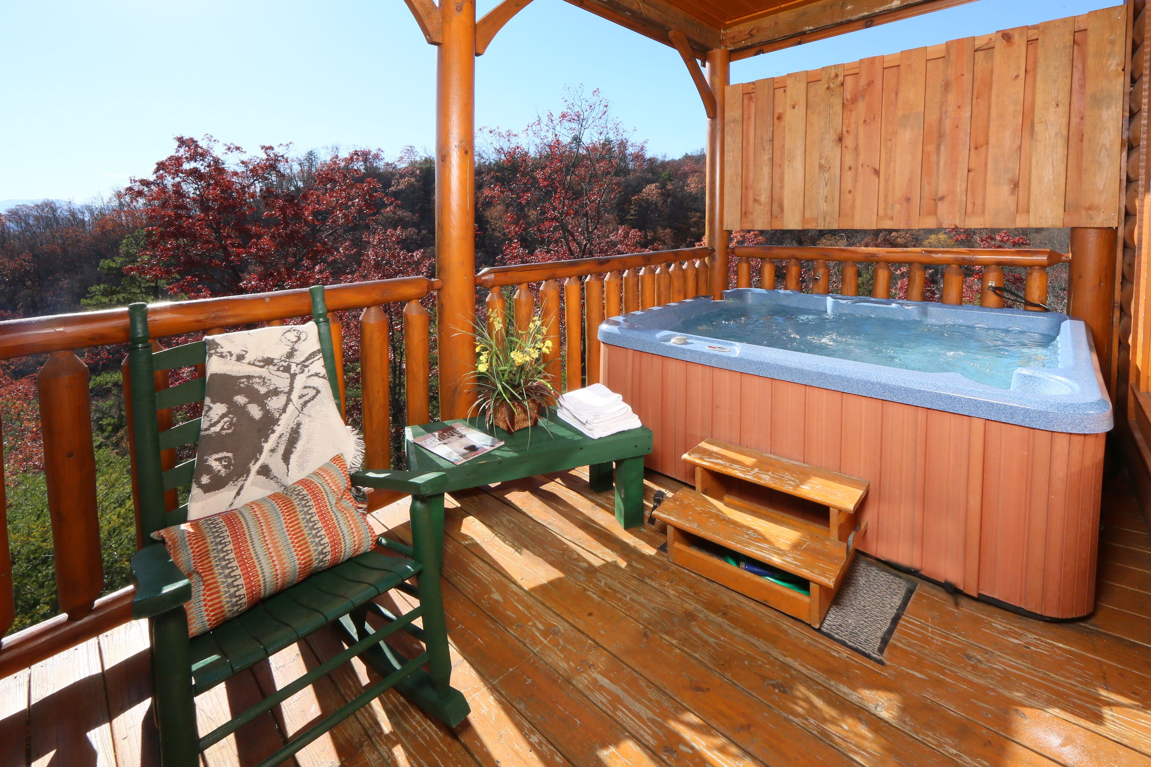 A wooden deck with a hot tub, a bench with a cushion, and a small table.