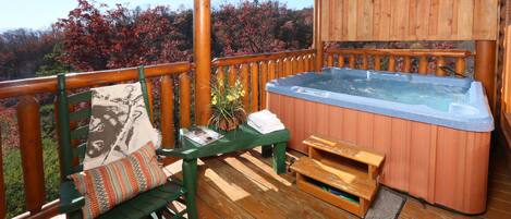 A wooden deck with a hot tub, a bench with a cushion, and a small table.