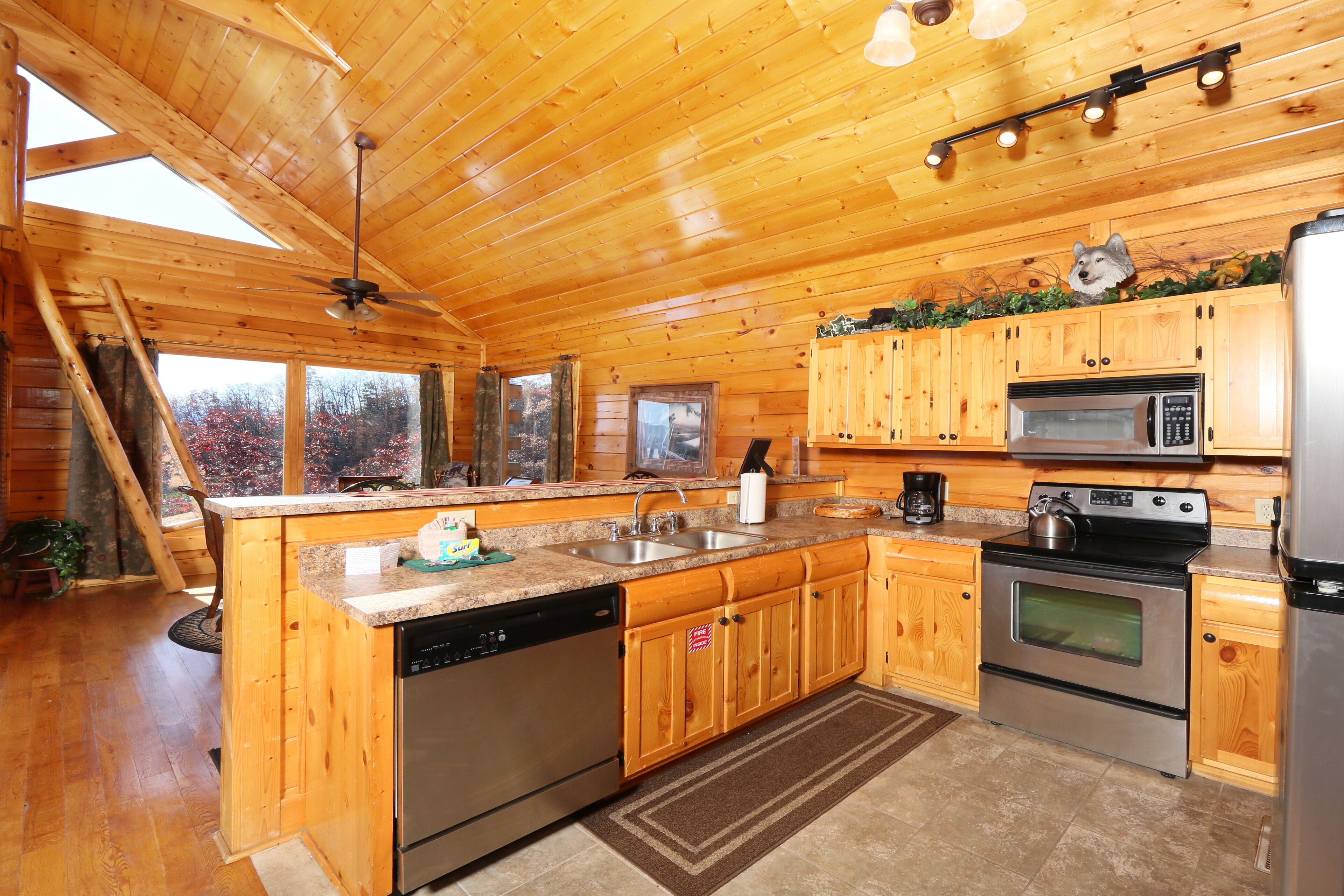 A wooden cabin kitchen with a dishwasher, stove, microwave, and a large island with a sink.