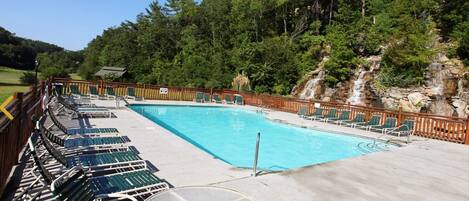 A rectangular swimming pool with a wooden deck, surrounded by lounge chairs and a table.