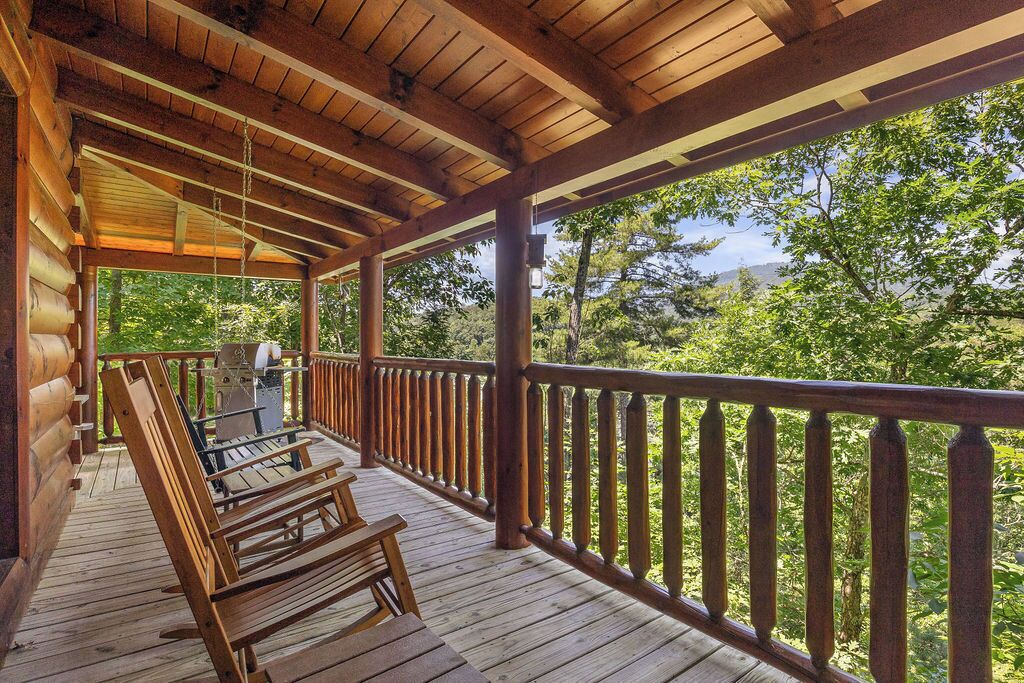 A wooden deck with a railing, wooden chairs, and a grill area.
