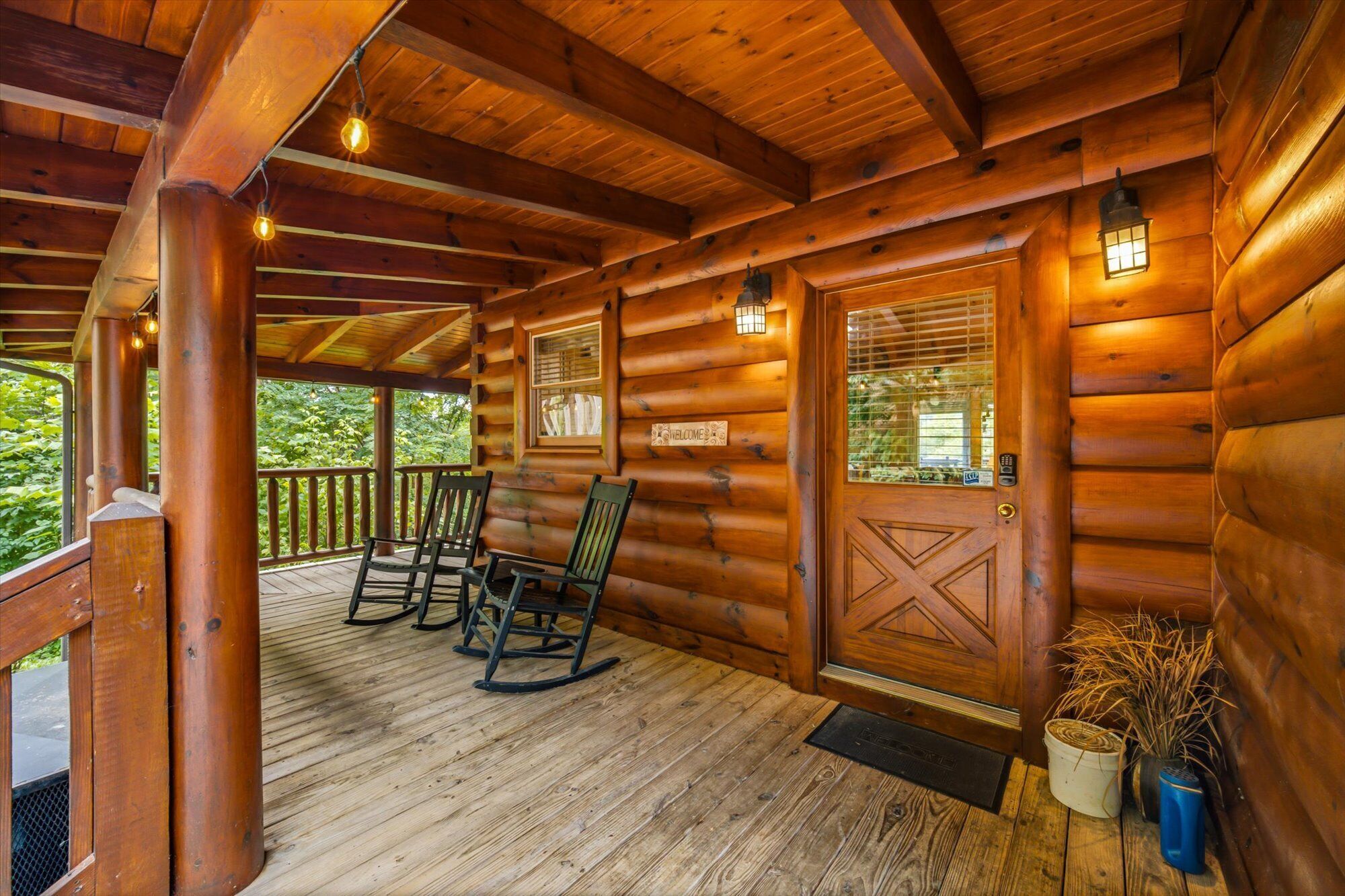 Una cabaña de madera con un porche, mecedoras y un letrero de bienvenida.