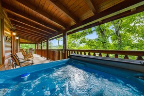 Una terraza de madera con un jacuzzi, con vista a un bosque frondoso y verde.
