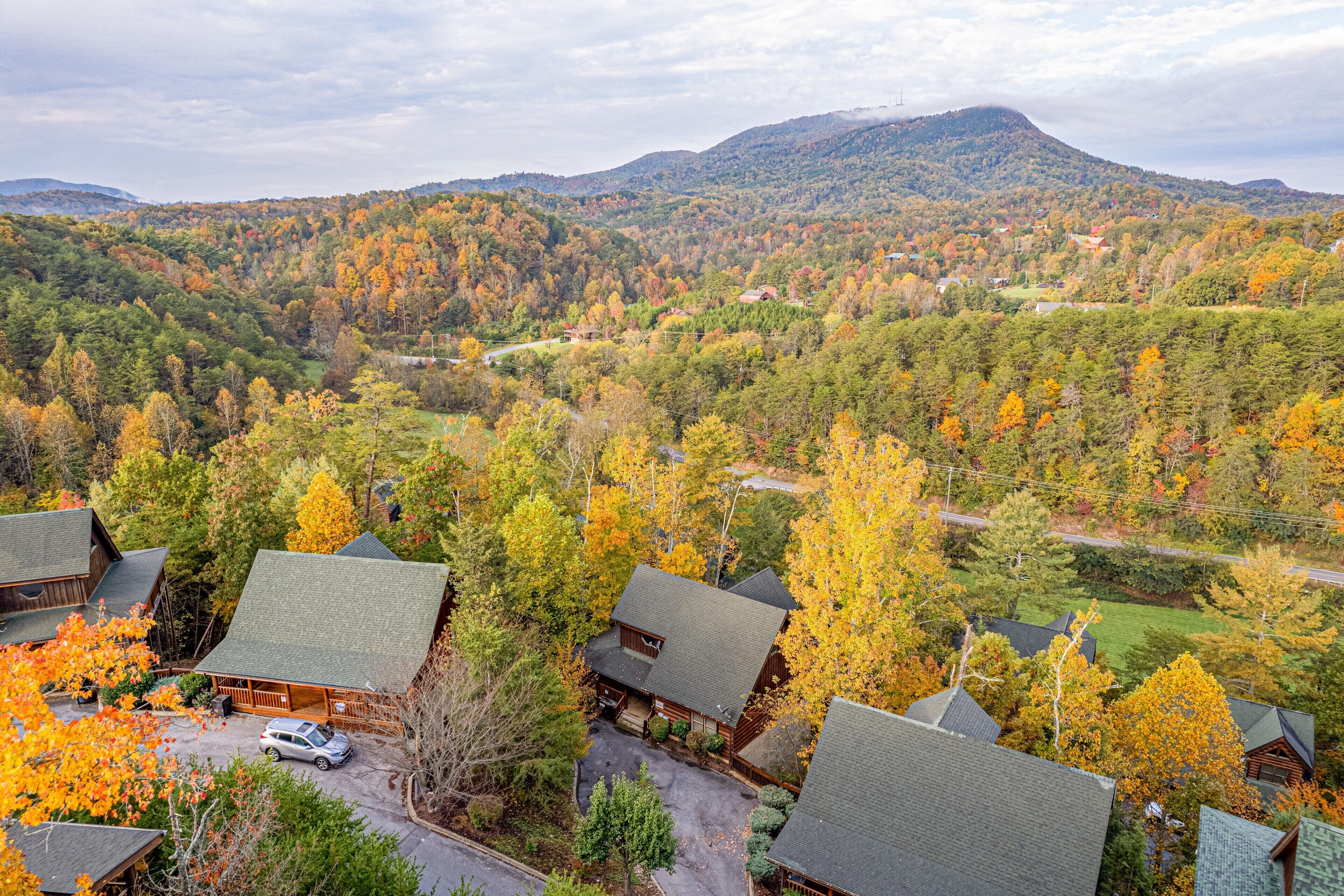 A lodge with multiple buildings, a parking area, and a view of a forested mountain range.