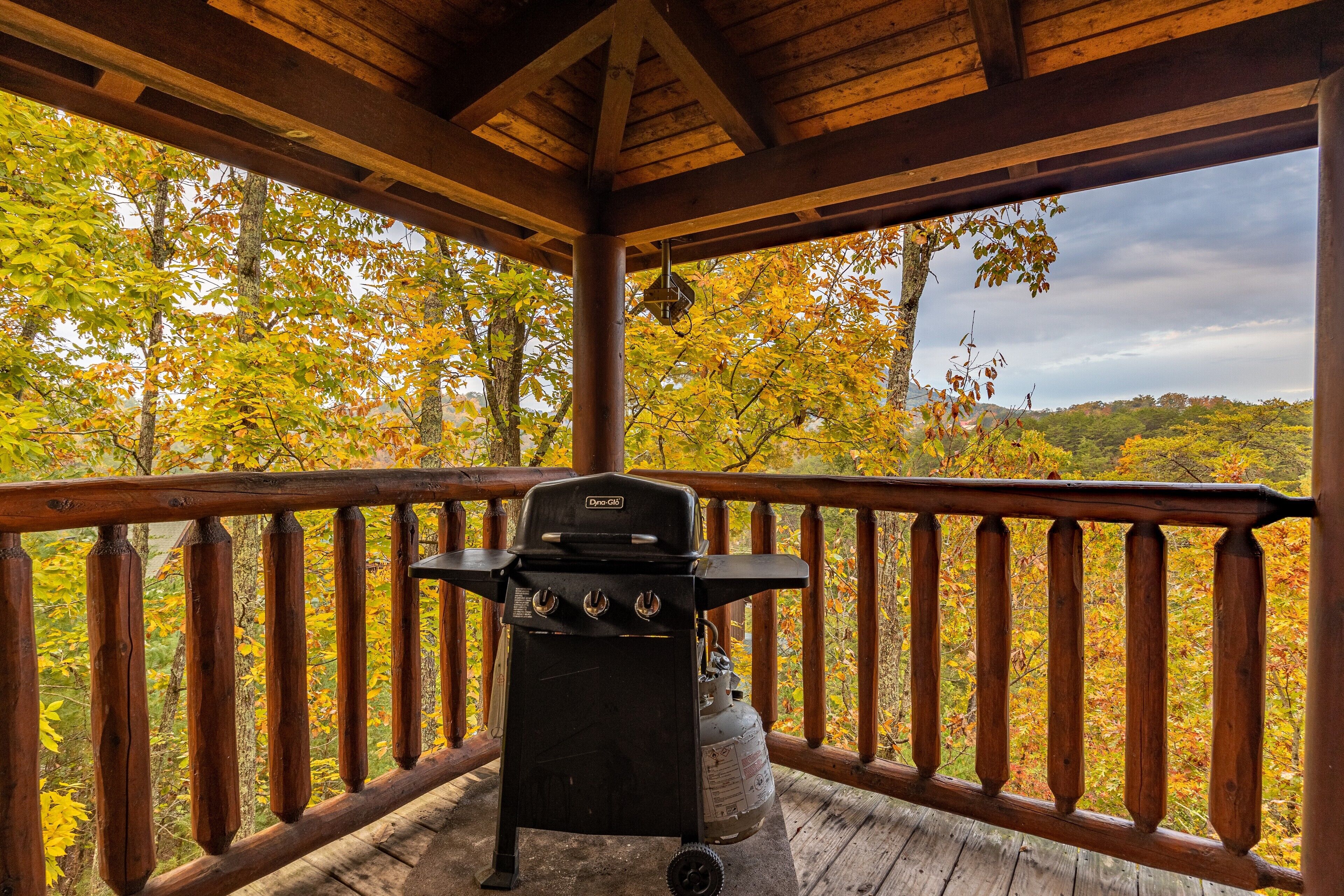 A covered outdoor grill area with a view of autumn foliage.