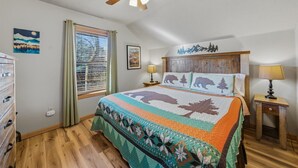 A bedroom with a wooden bed, a ceiling fan, a window with blinds, a dresser, and a wall with a mountain-themed picture. - Divine Escape - Two Bedroom Chalet (Gatlinburg)