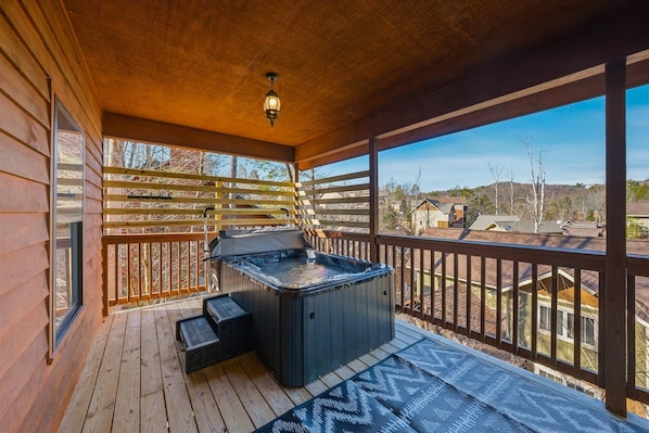 Una terraza de madera con un jacuzzi, una pérgola y vistas a una zona residencial.
