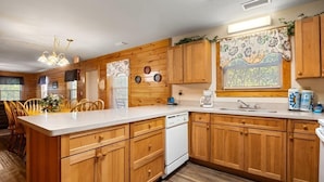A kitchen with wooden cabinets, a white countertop, a dishwasher, and a window with floral curtains. - Poplar Point Condo Unit 12E - Three Bedroom Condo (Pigeon Forge)