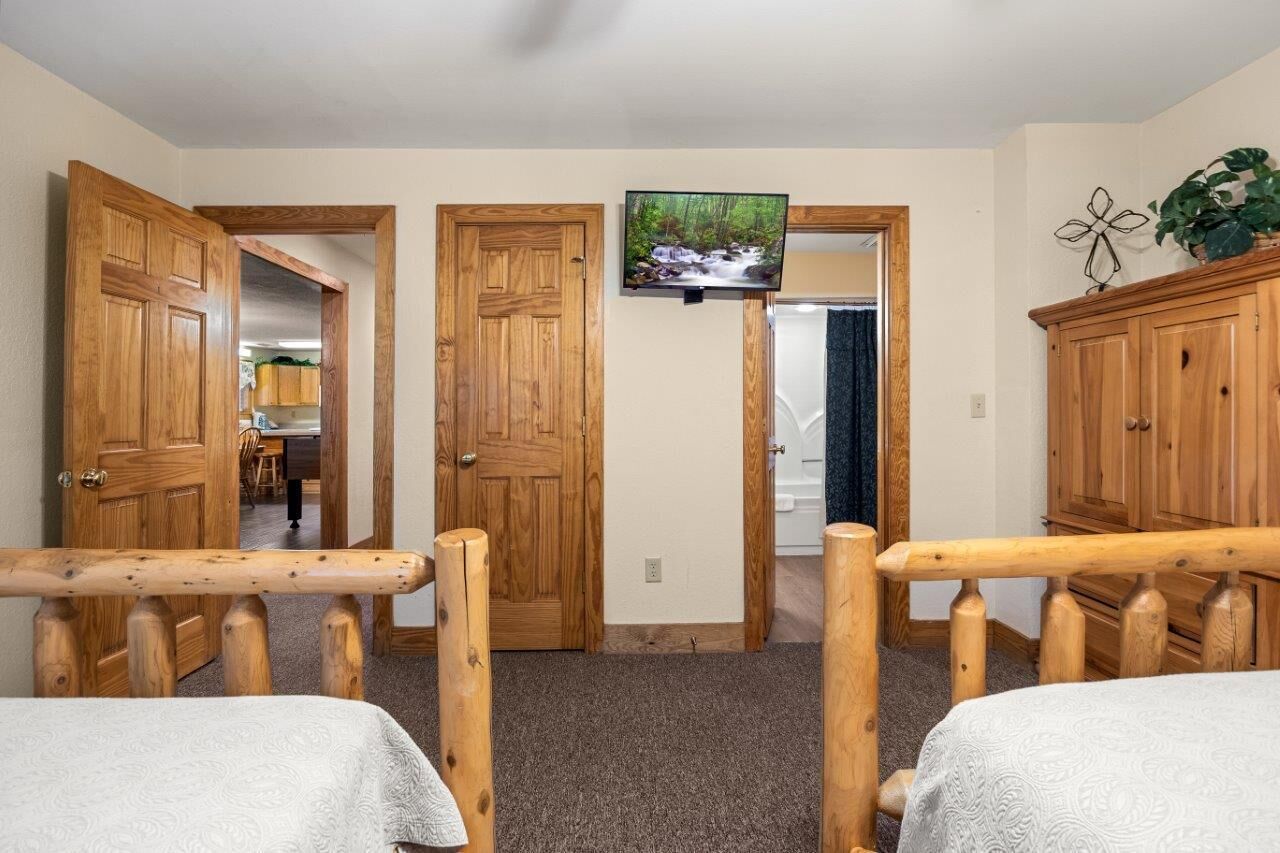 A room with two wooden beds, a television mounted on the wall, and a wooden cabinet.