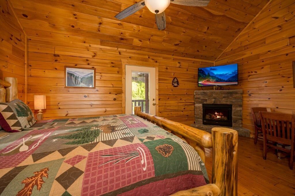 Ein gemütliches Blockhaus-Zimmer mit Bett, Kamin, Fernseher und einer Tür, die nach draußen führt.