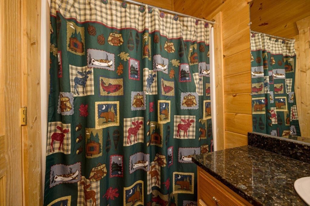 A bathroom with a wooden interior, a green and plaid shower curtain, and a granite countertop.