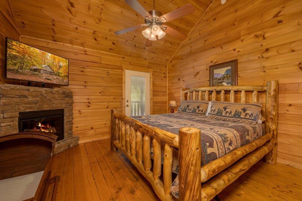 Un dormitorio tipo cabaña de troncos con chimenea de piedra, estructura de cama de madera y ventilador de techo.