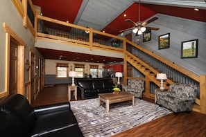 A spacious living area with a black leather sofa, patterned armchairs, a wooden coffee table, and a red ceiling. A staircase with wooden railings leads to an upper level. - Firefly Nights - Five Bedroom Chalet (Gatlinburg)