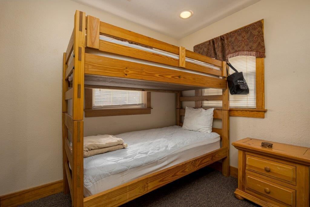 A bunk bed with a wooden frame, a bedside table, and a window with blinds.