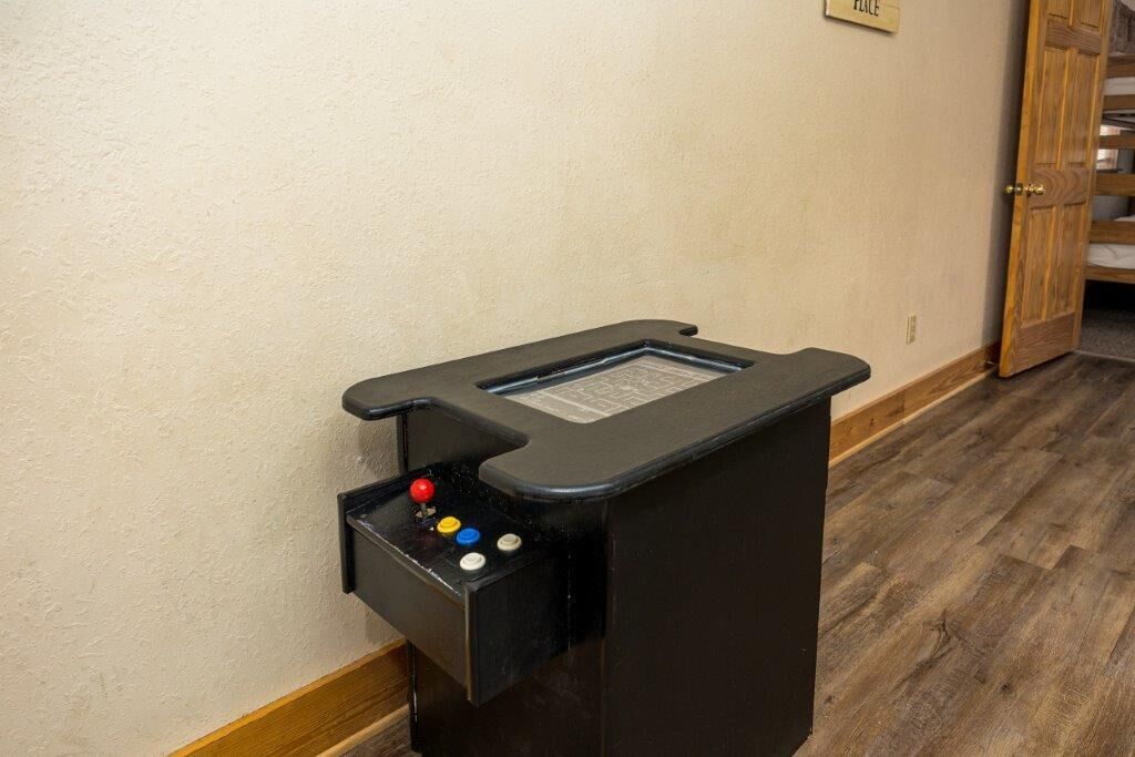 A black console with a joystick and buttons, likely for a game or interactive feature, mounted on a wall in a room with wooden flooring and a door in the background.