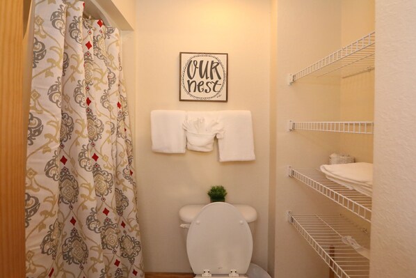 Un baño con inodoro, cortina de ducha, toallero con una toalla blanca y un cartel en la pared que dice 'OUR REST'.