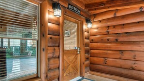 A wooden cabin entrance with a large window, a door with a cross design, and two wall-mounted lanterns. - Mayberry - Three Bedroom Cabin (Sevierville)