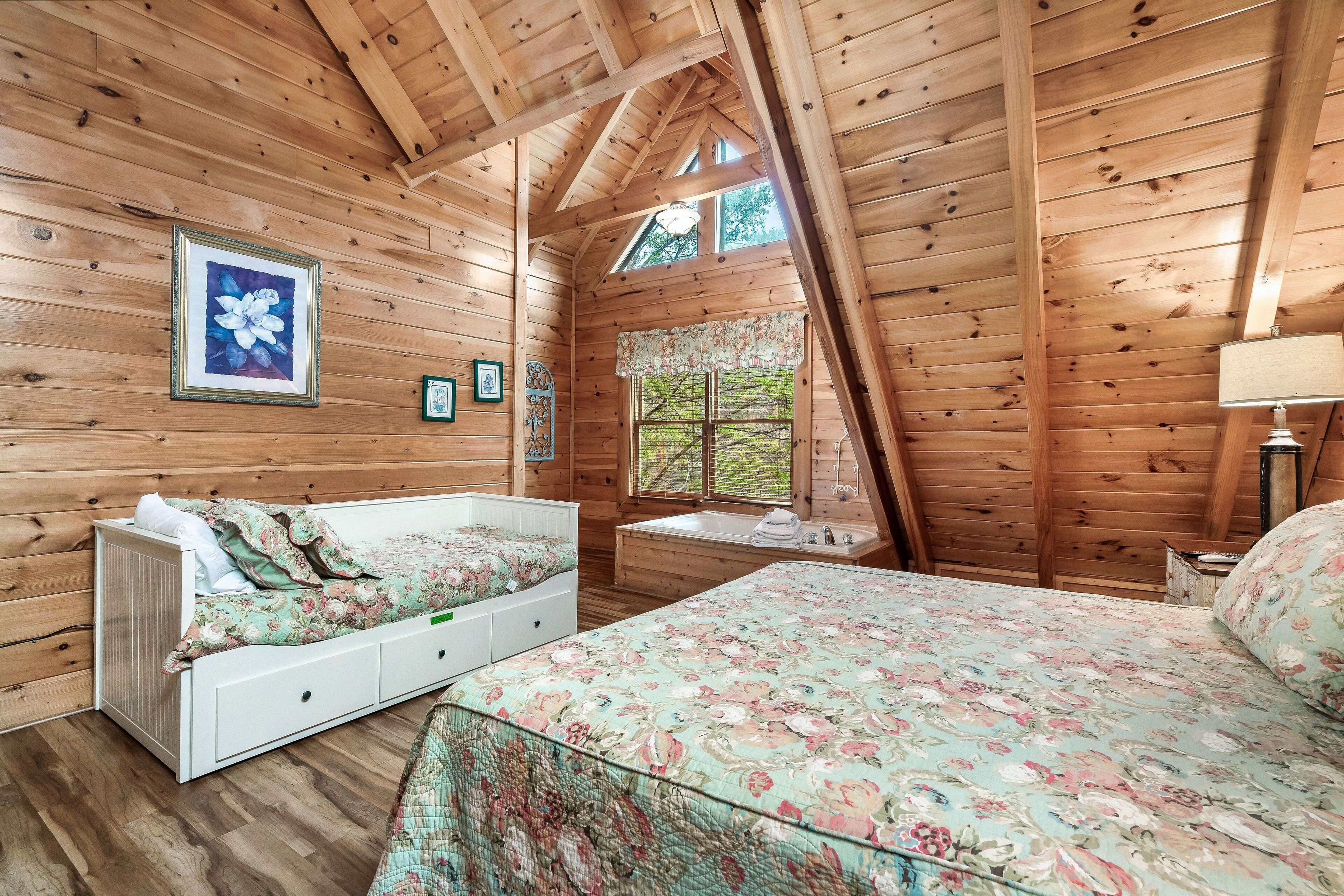 A wooden cabin bedroom with a bed, a bench, a window, and a framed picture on the wall.