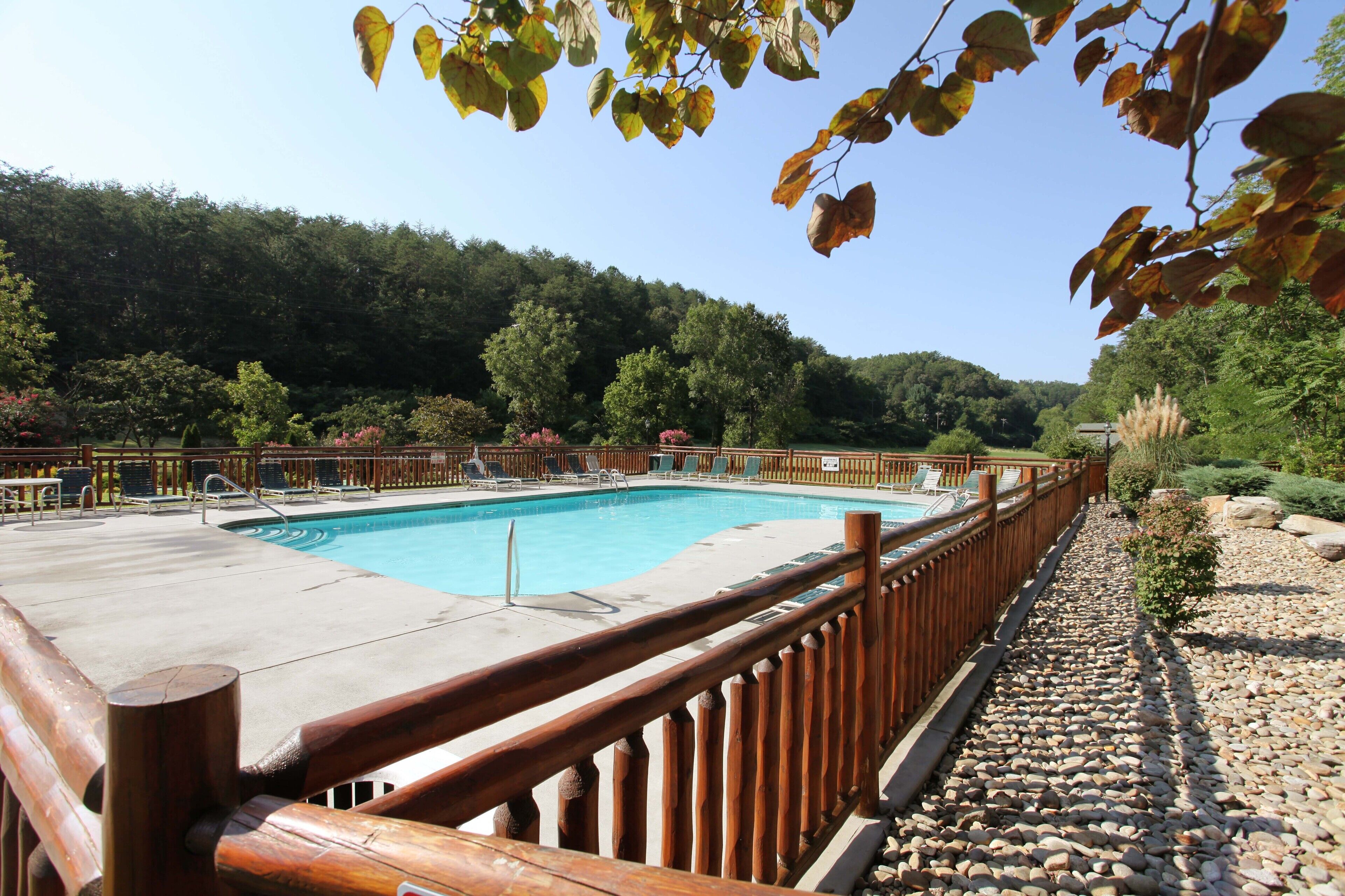 A pool area with a wooden fence, surrounded by trees and a clear sky.