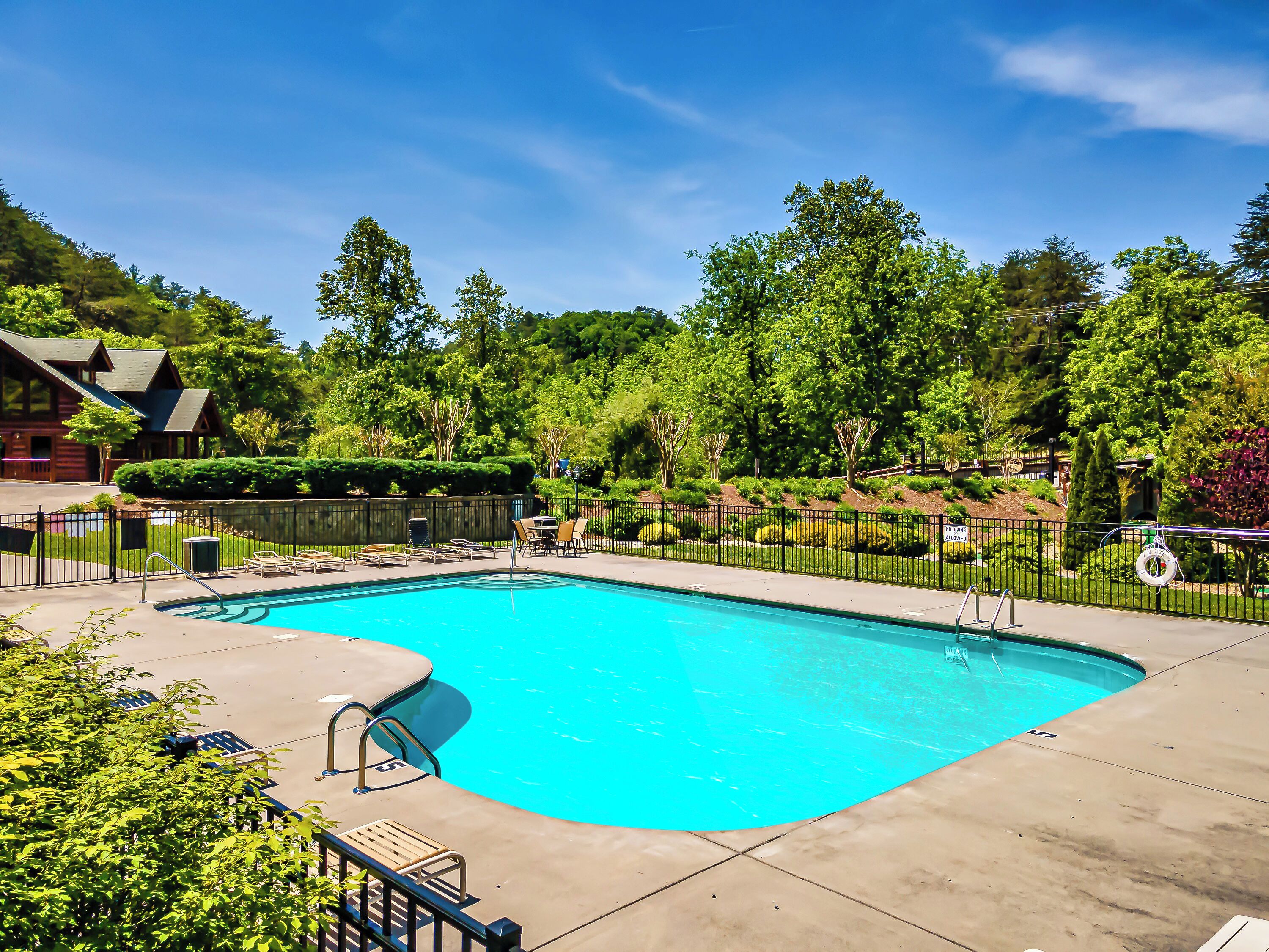 A swimming pool with a curved edge, surrounded by a fence, and adjacent to a building with a sloped roof.