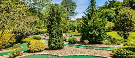 A miniature golf course with multiple green putting areas, surrounded by various trees and shrubs.