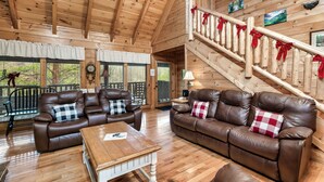 A wooden interior with two leather sofas, a wooden coffee table, and a staircase with red bows. - Mayberry - Three Bedroom Cabin (Sevierville)