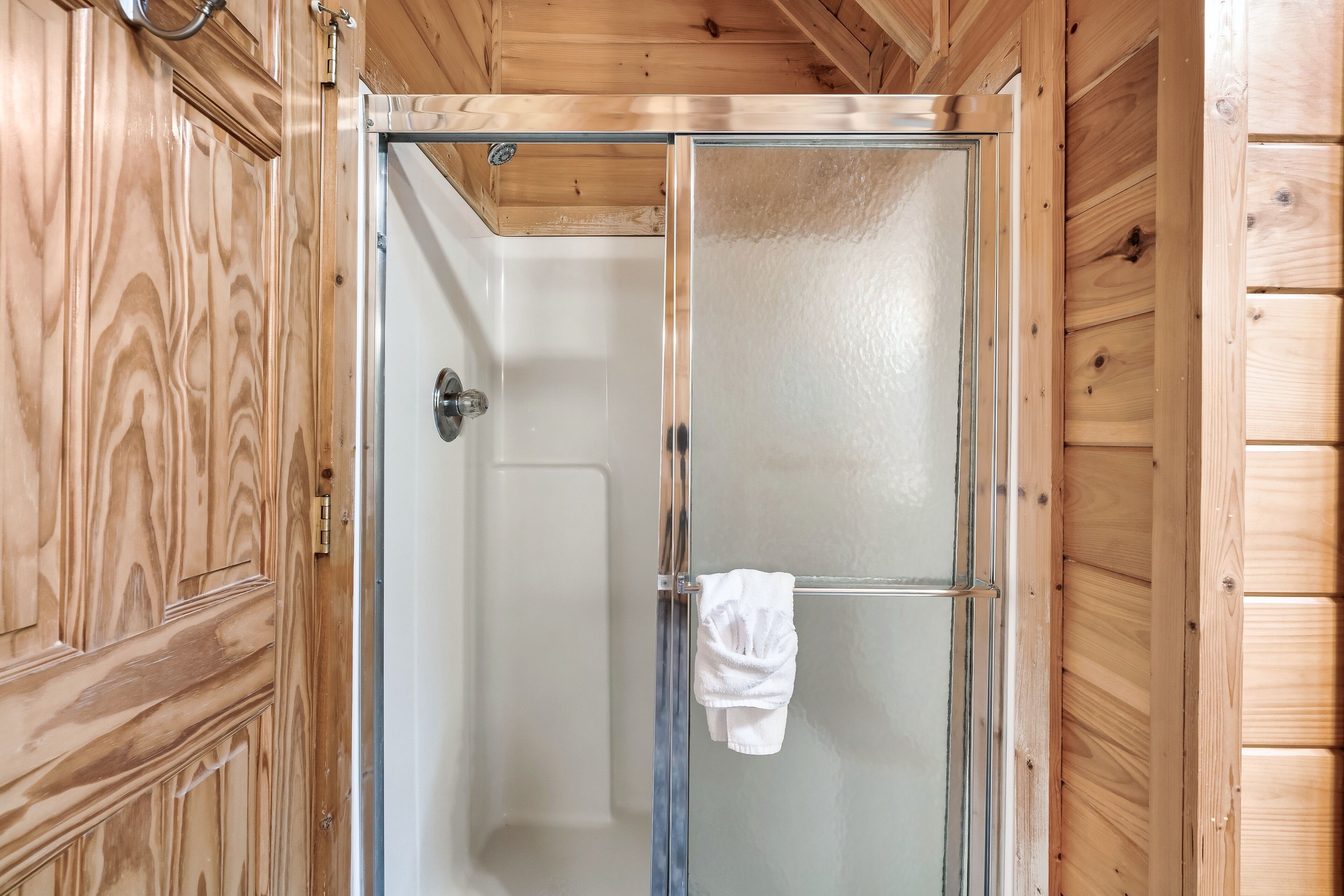 A wooden-paneled room with a glass shower enclosure and a towel hanging on the door.