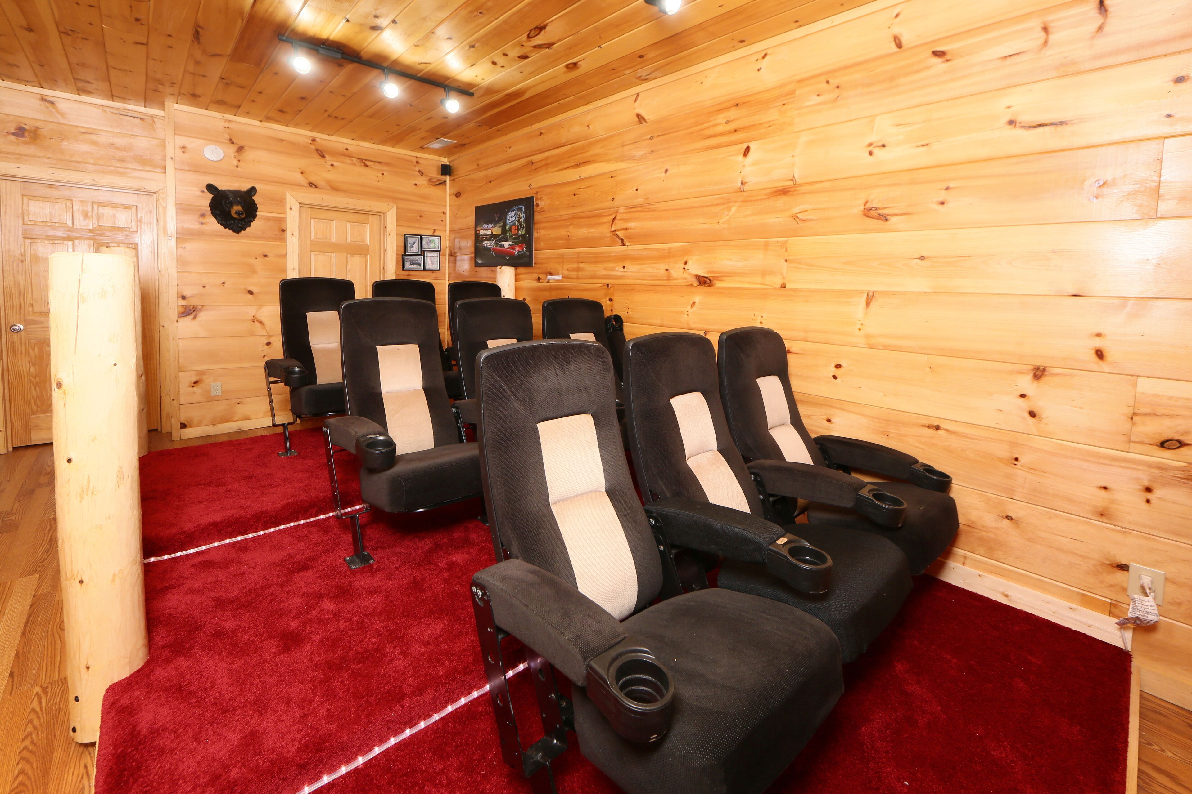 Une rangée de fauteuils noirs et blancs, dotés d’accoudoirs et d’un rembourrage confortable, est disposée sur un tapis rouge dans une cabane en bois. Une tête d’ours empaillée est accrochée au mur.